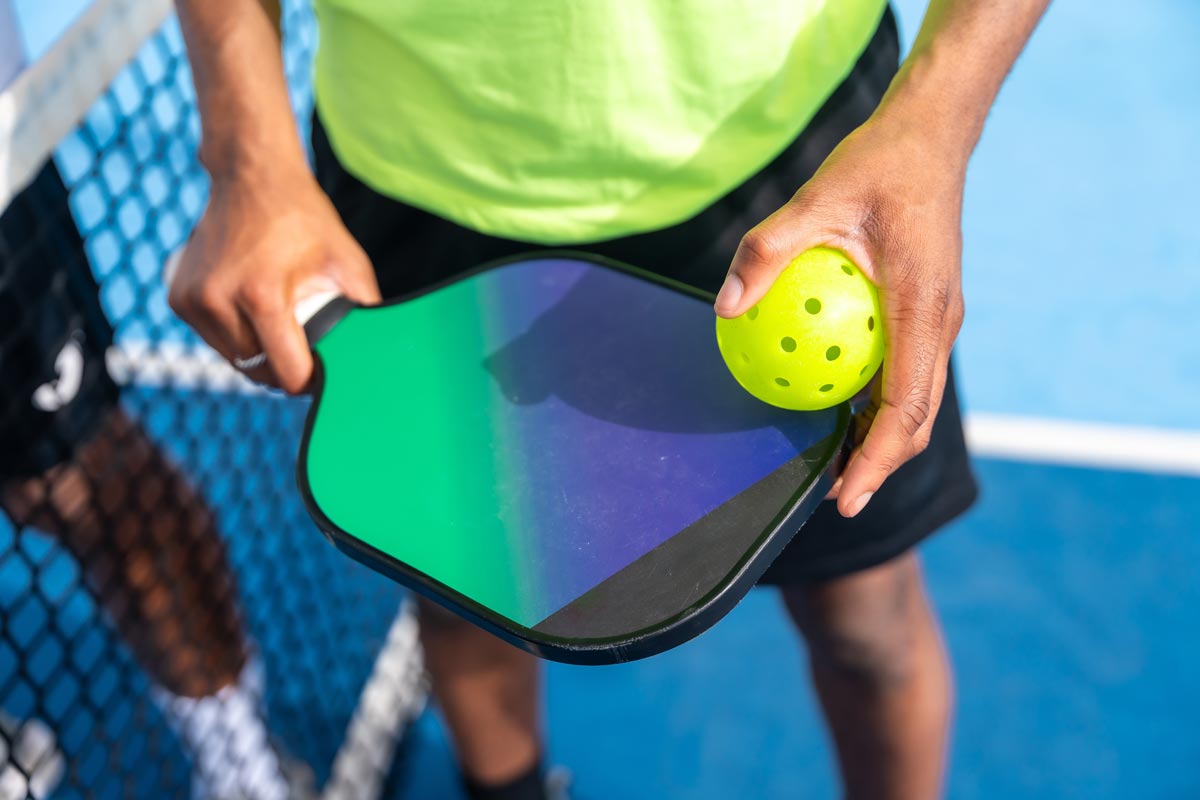 A pickleball player holds a ball and paddle on the court.