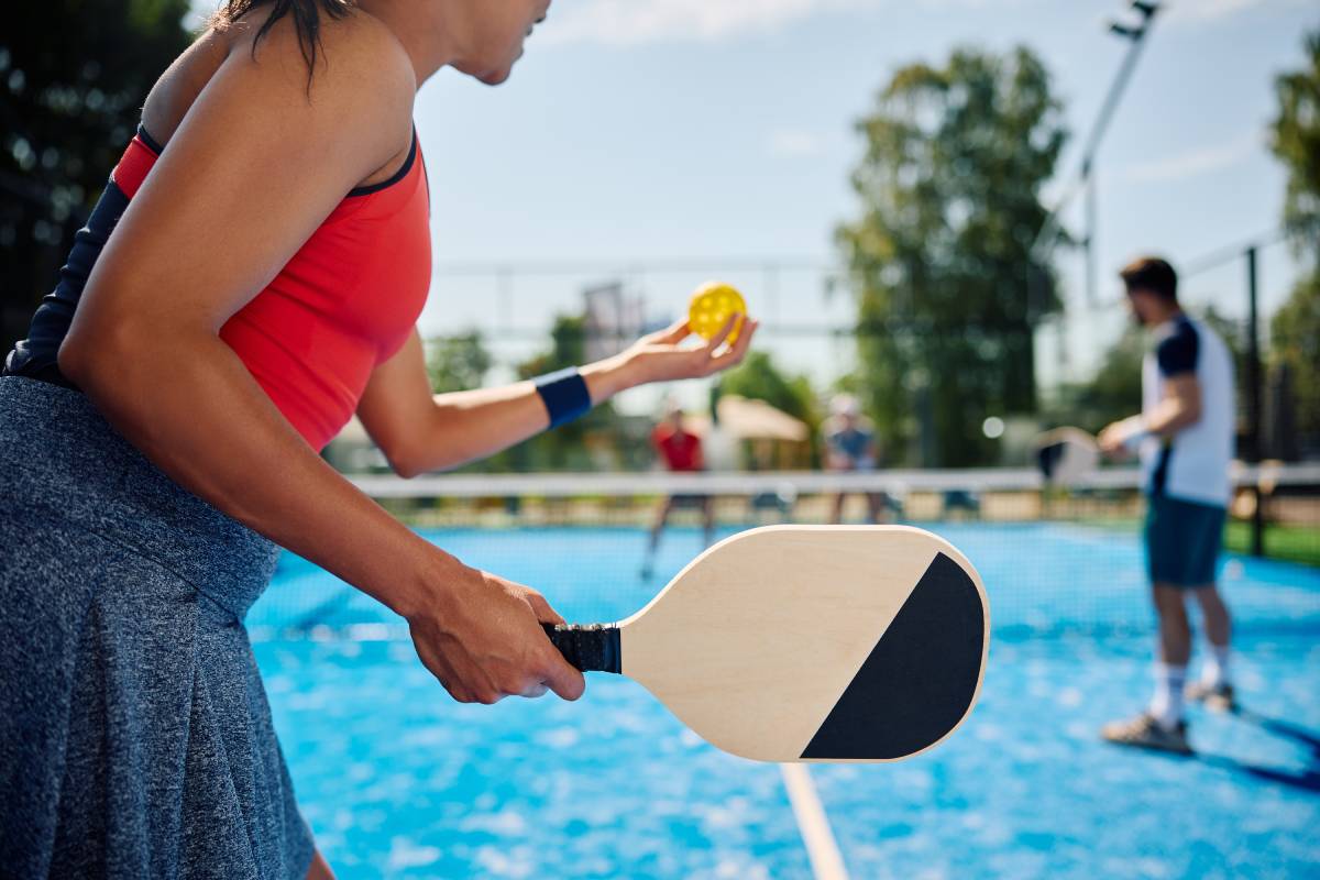 A woman serving the ball in a pickleball game.