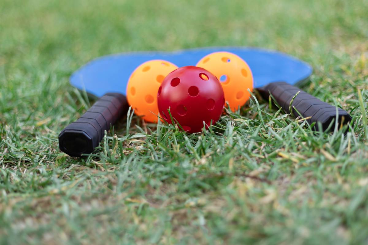 Pickleball paddles and balls sit on a grass surface.
