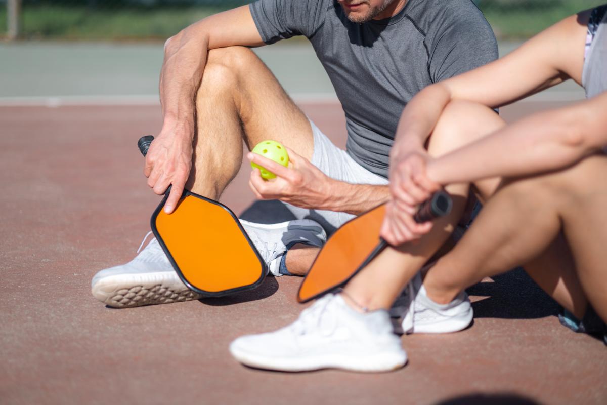 Two pickleball players sit and talk strategy on a court between games.