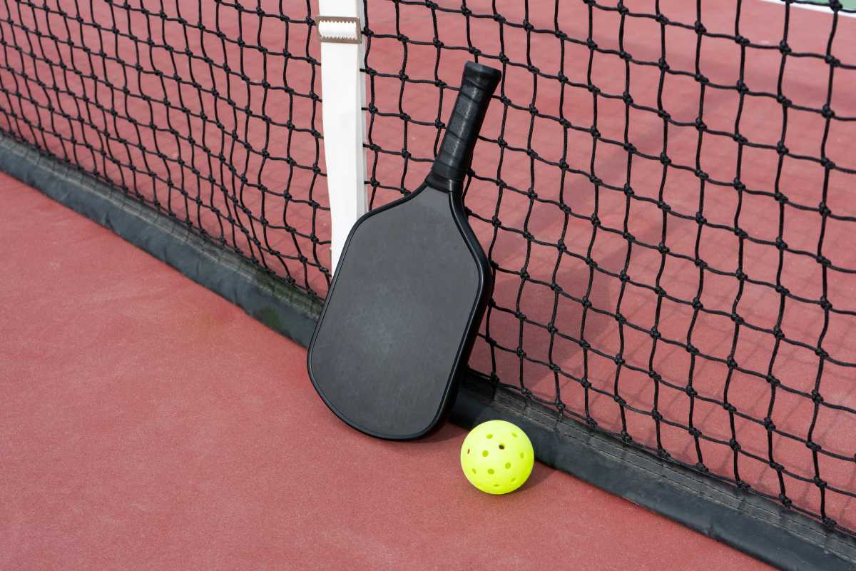 A pickleball paddle and ball rest in front of a net on a court.