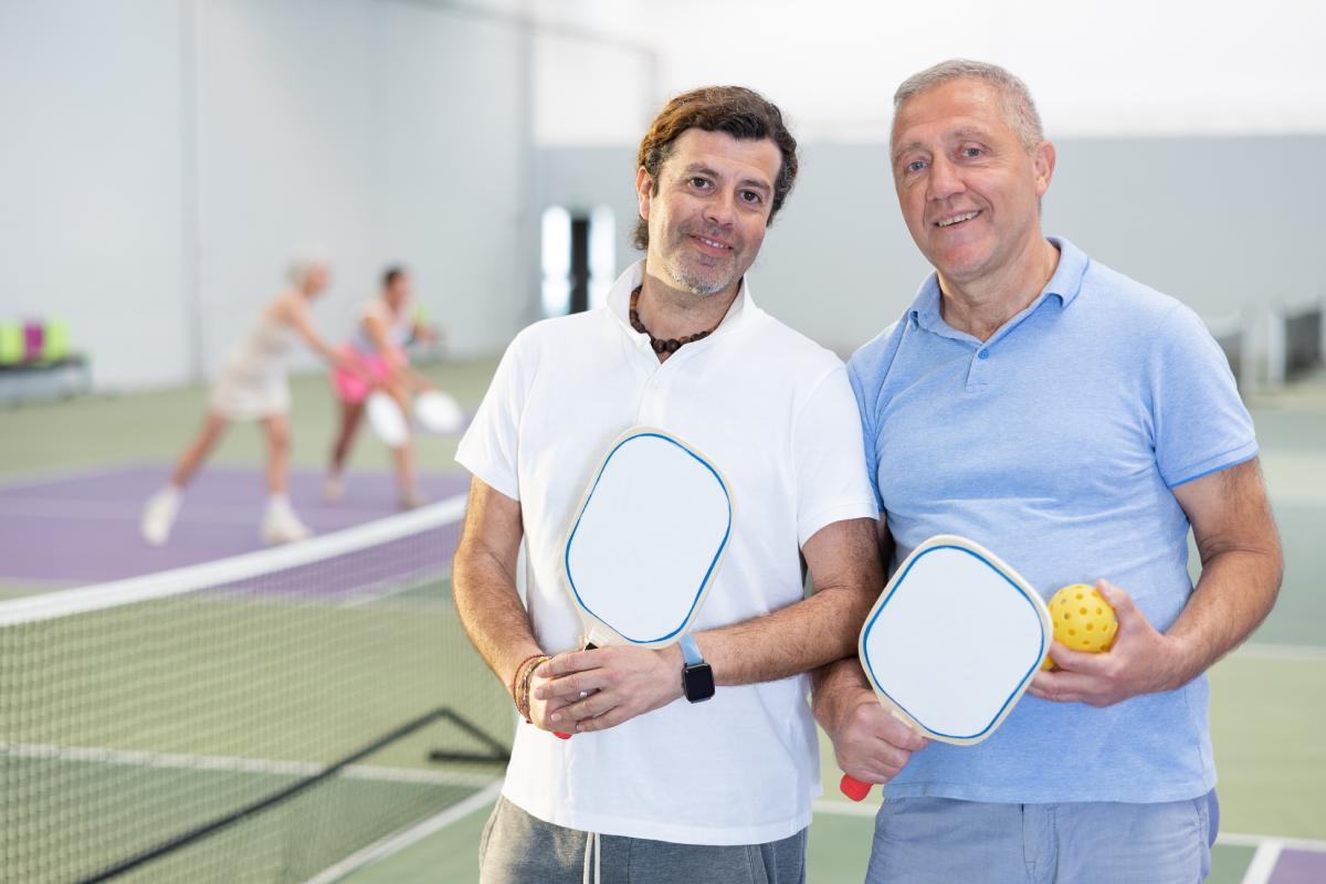 A pickleball player and coach stand together on the court. 