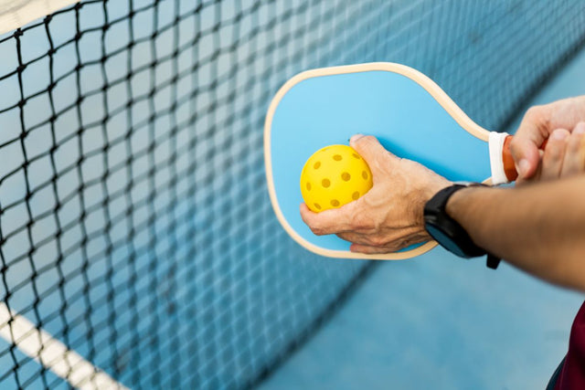 A pickleball player holds the ball to their paddle.