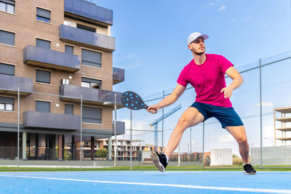 Man plays pickleball in a pink shirt and blue shorts