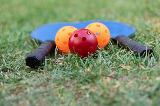 Pickleball paddles and balls sit on a grass surface.