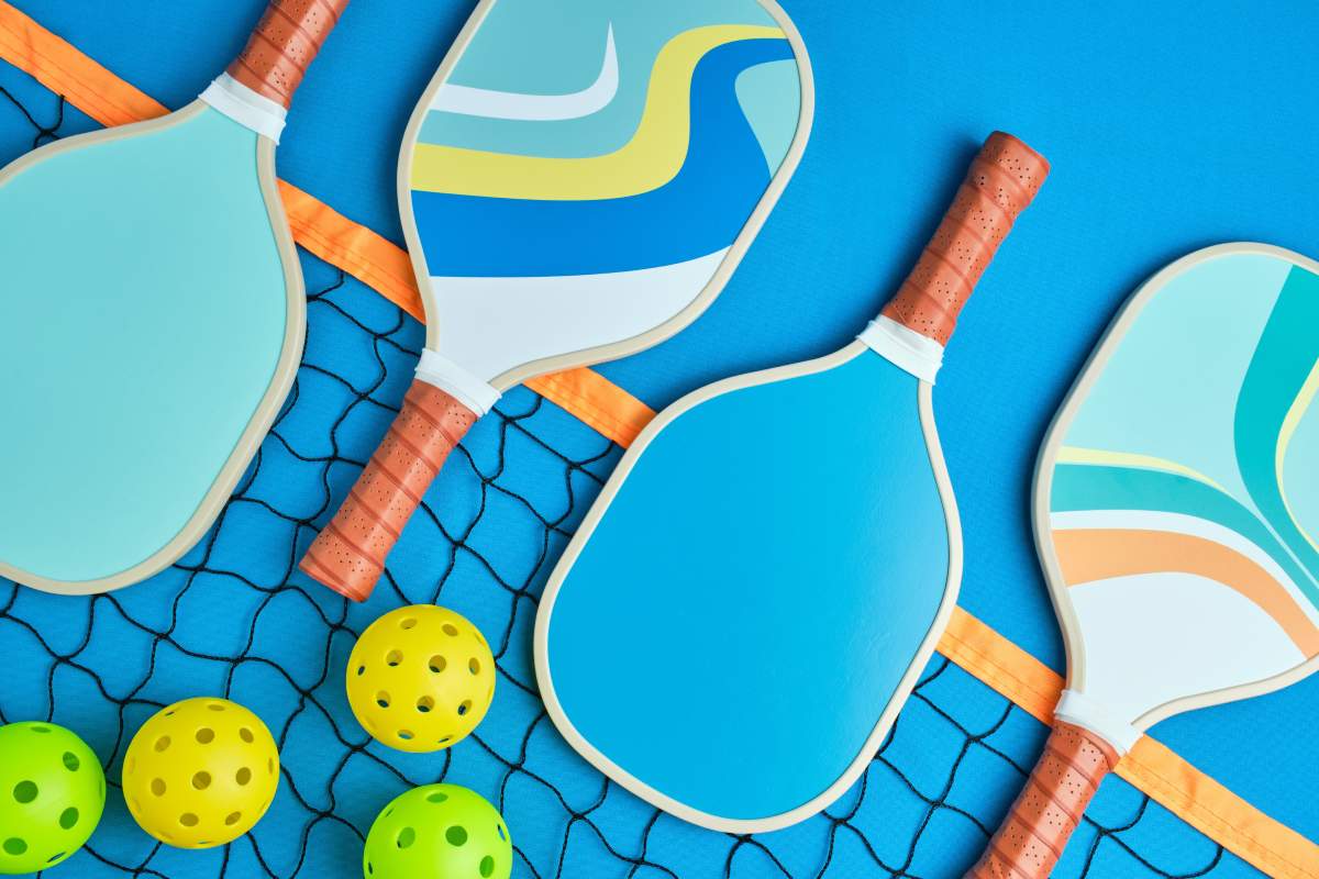 Pickleball paddles, balls, and a net seen against a blue background. 